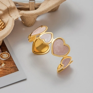 Detailed shot of gold heart-shaped segments with pink marble enamel on an open cuff bracelet