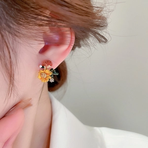 Detail of yellow flower and red berry stud earrings with rhinestones on model's ear