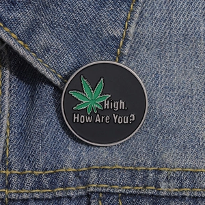 Macro shot of High How Are You enamel pin on denim jacket featuring green leaf design