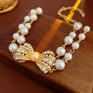 Close-up of double-layer gold pearl bracelet with crystal bow and orange centerpiece