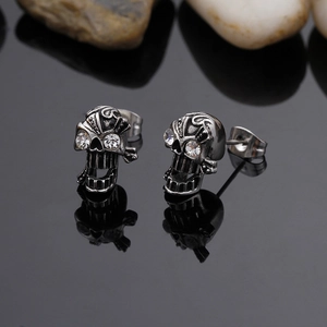 Close-up of gothic skull stud earrings with sparkling white crystals on black reflection