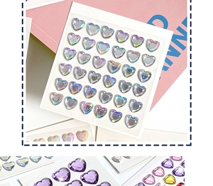 Detail of 3D heart-shaped crystal gem stickers with colorful laser finish on pink paper