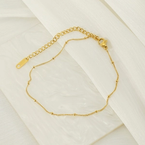 Elegant gold titanium steel anklet with side bead chain on white marble background