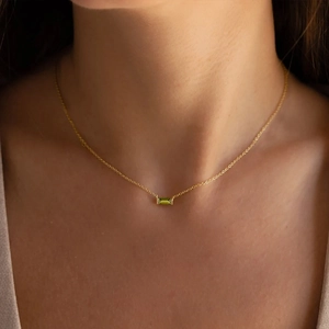 Close-up of minimalist gold necklace featuring a rectangular green gemstone pendant on model