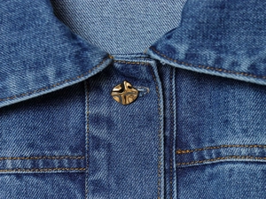 Détail du col d'une chemise en jean bleue avec un bouton métallique doré en croix