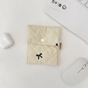 Detailed macro view of quilted beige mini pouch featuring black bow embroidery and button
