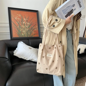 Detail of beige corduroy tote bag with bear embroidery and metal buckle closure