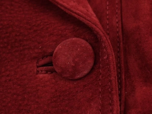 Close-up of deep red suede fabric texture with matching circular button and stitching