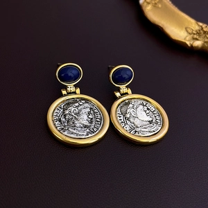 Close-up of vintage coin earrings with gold and silver tones and deep blue gemstone