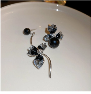 Detail of asymmetric black flower earrings with dark pearls and silver streamline design