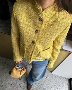 Close-up of the yellow tweed texture and button detail on a stylish women's jacket