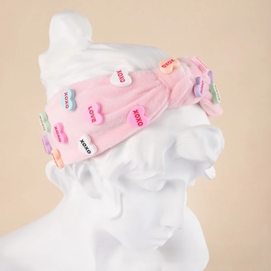 Pink plush knotted headband with colorful XOXO heart charms on a model head