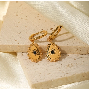 Detail of gold teardrop earrings with black gemstones on textured stone and silk