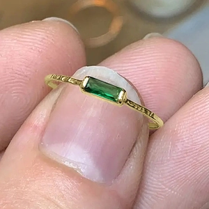 Macro detail of rectangle green gemstone and hammered texture on gold finish ring band