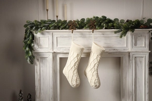 Close-up of white cable knit Christmas stockings hanging on a festive decorated mantel