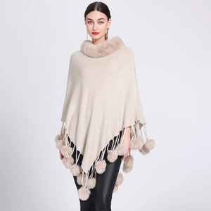 Detail of beige knit poncho featuring faux rabbit fur collar and playful pom-poms