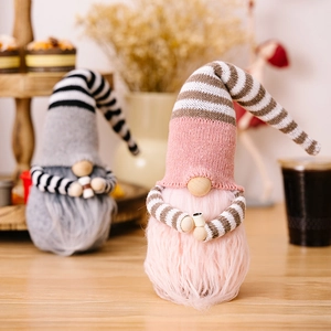 Close-up of pink and grey striped Christmas gnomes holding coffee cups on a cozy table