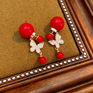 Macro shot of vintage butterfly pearl earrings with red resin beads on dark textured fabric
