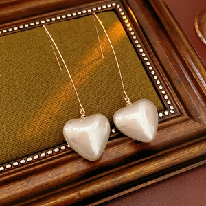 Detail of vintage heart pearl drop earrings on green velvet with golden hooks