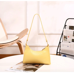 Detail view of the yellow crocodile pattern underarm bag on a white table
