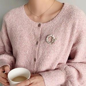 Elegant round pearl brooch with diamond butterfly on a pink knitted cardigan