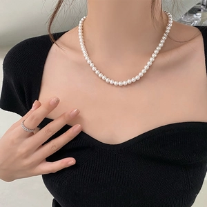 Classic white pearl necklace on model with black square neck top showing elegant texture