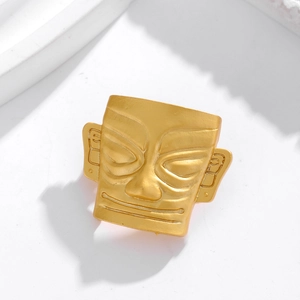 Macro detail of golden metal Sanxingdui mask brooch with ancient textured finish