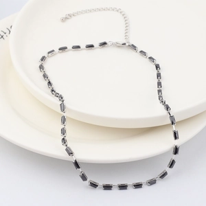 Détail d'un collier avec pierre rectangulaire noire et chaîne argentée sur des plats