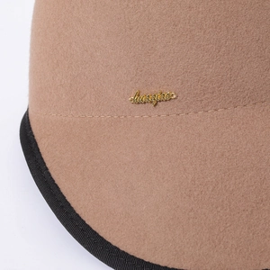 Macro shot of camel wool felt cap featuring black ribbed trim and gold metal logo