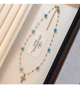 Macro detail of gold beaded cross necklace with blue stone accents on a display card