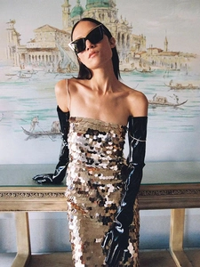 Detailed view of shimmering gold sequins on a strapless dress with long black gloves