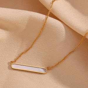 Macro d'un collier barre plaqué or 18K avec nacre blanche sur tissu en soie champagne