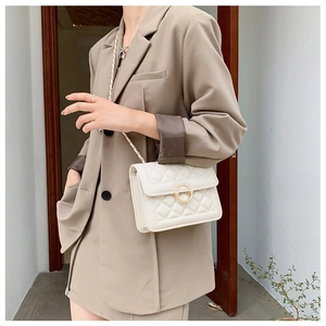 Quilted crossbody bag with pearl buckle and chain strap shown on model's shoulder