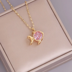 Cute 18K gold fish pendant necklace with a round pink zircon on a beige jewelry cushion