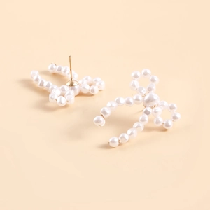 Detailed view of handmade bow earrings made of white pearls with golden pins
