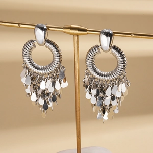 Détail de boucles d'oreilles argentées à pompons avec anneaux texturés et sequins goutte d'eau