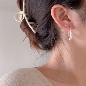 Detail view of irregular silver U-shaped earring and beige hair claw on model