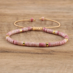 Detailed close-up of pink emperor stone beads with gold spacers on wood background