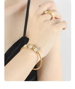 Detailed close-up of a gold twist bangle and a woven ring with pearls on a model wrist