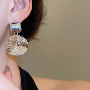 Close-up of a silver textured round pendant earring worn on a model's earlobe