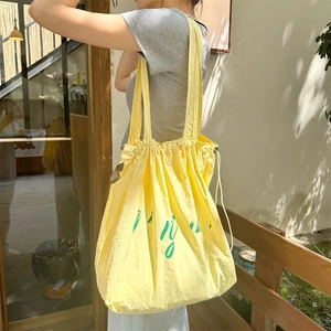 Detail of yellow nylon drawstring tote bag with green Bonjour text on a model's shoulder