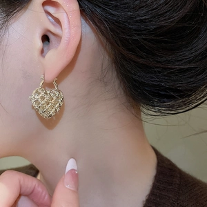 Close-up of a gold hollow heart-shaped earrings featuring a delicate woven metal texture
