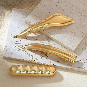 Elegant gold minimalist irregular spring hair clips displayed on decorative beige stones