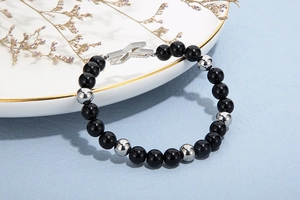 Detail of beaded bracelet with silver hollow cross pendant on a white ceramic plate