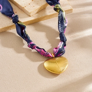 Detail of gold heart pendant with radial texture on a blue floral silk ribbon necklace