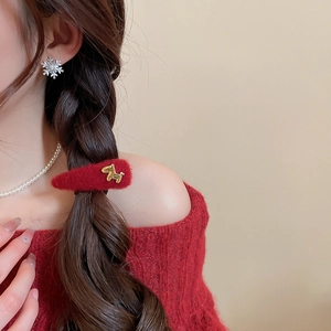 Detail showing a red plush hair clip with gold animal accent and silver snowflake earrings