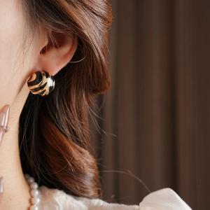 Detail of round spiral earring in gold and black on model against a brown background