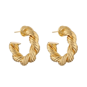 Close-up of golden hollow twisted C-shape earrings with a polished metallic finish