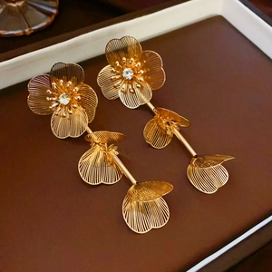 Détail de boucles d'oreilles dorées à fleurs superposées avec cœurs en zircon