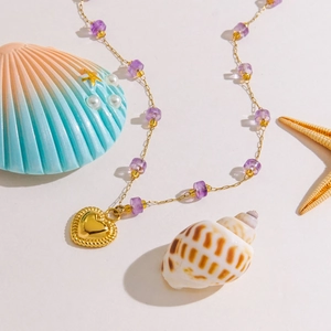 Golden chain necklace with purple heart pendant and amethyst beads on ocean summer background